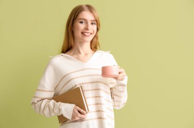 Yeşil arka planda bir fincan çay ve kitapla güzel genç bir kadın.