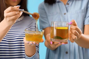 Mavi arka planda cam çay ve bal taşıyan genç kadınlar, yakın plan.