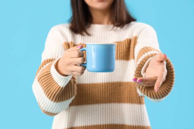 Mavi arka planda çay fincanı olan genç bayan, yakın plan.