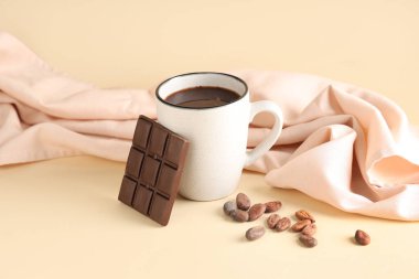 Bej arka planda kakao çekirdeği ve kumaşlı bir fincan lezzetli sıcak çikolata.