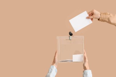 El, oy pusulasını bej arka plandaki oy sandığına koyuyor. Seçim kavramı