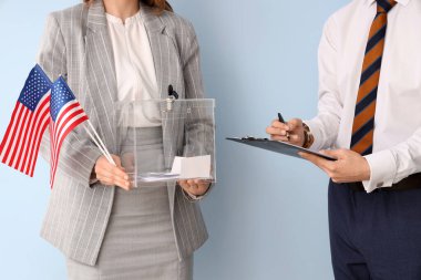 Elinde oy sandığı olan kadın ve ABD bayrakları arka planda panoda yazılı oy pusulası olan adamın yanında. Seçim kavramı