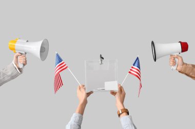 Eller oy sandığını tutuyor, beyaz arka planda Amerikan bayrakları ve megafonları var. Seçim kavramı