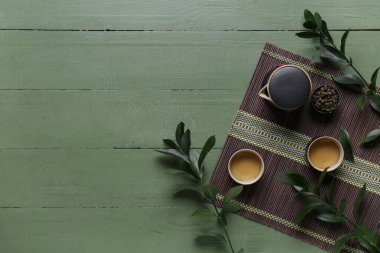 Bambu hasırı, fincanlar dolusu lezzetli çay, çaydanlık ve yeşil yapraklı kase.