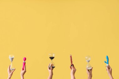 Sarı arka planda kum saatleri ve vibratörler tutan kadın eller.