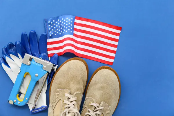 Industrial stapler, boots, gloves and USA flag on blue background. Labor Day celebration