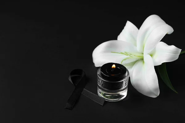 Beautiful lily flower with funeral ribbon and candle on black background