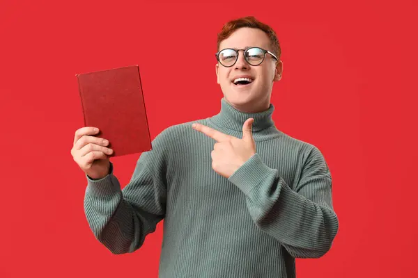 Emotionaler Junger Mann Zeigt Auf Buch Auf Rotem Hintergrund — Stockfoto