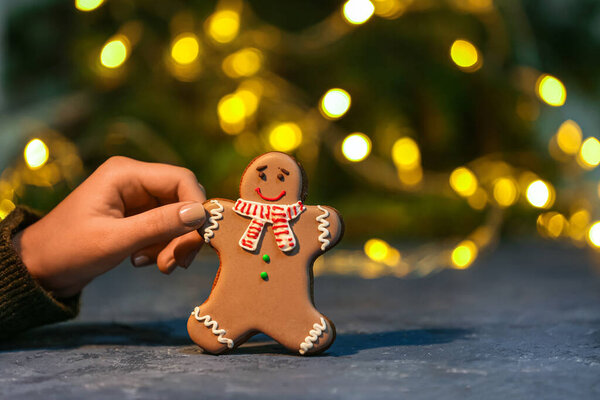 Рука женщины со сладким рождественским печеньем на столе против размытых огней