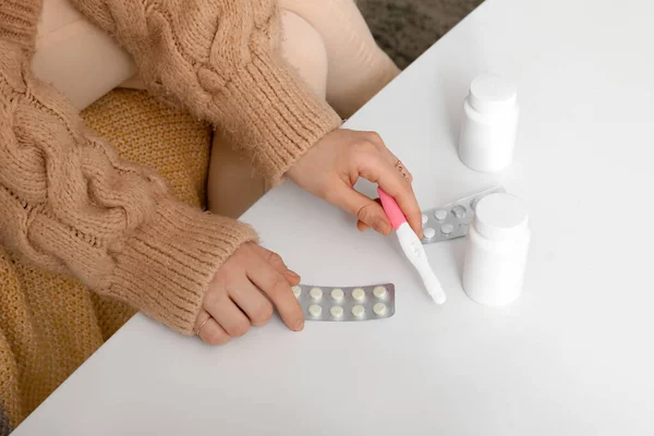 Woman with pregnancy test and pills on table at home, closeup