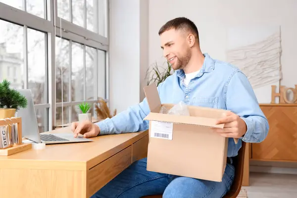 Young man with open parcel using laptop at home