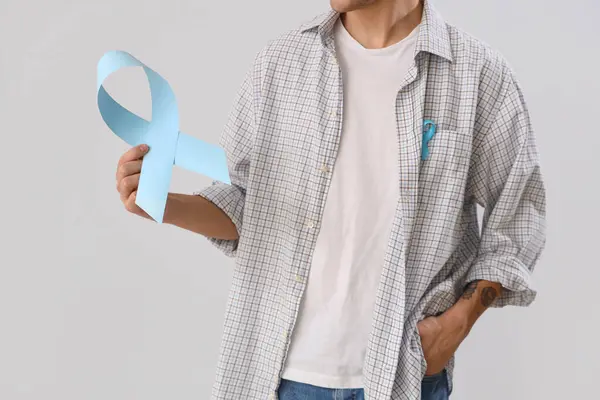 Young man with blue ribbons on light background, closeup. Prostate cancer awareness concept