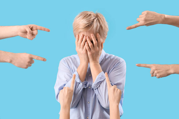 People pointing at mature woman covering her face on blue background. Accusation concept