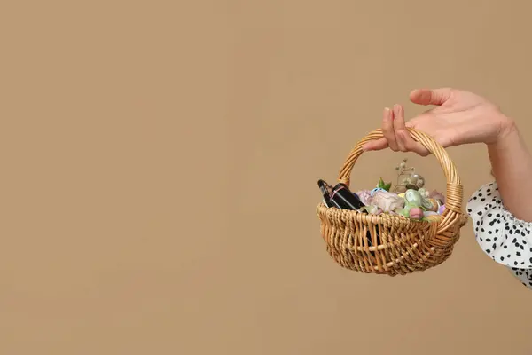 Woman holding Easter basket with decorative cosmetics on color background
