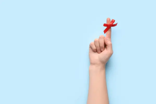 Female hand with red bow on index finger against blue background. Reminder concept