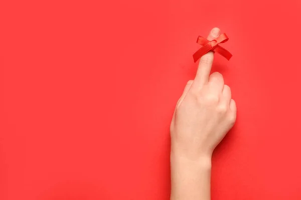 Female hand with red bow on index finger against red background. Reminder concept