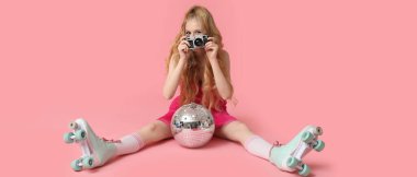 Pembe arka planda eski paten, disko topu ve fotoğraf makinesi olan güzel genç bir kadın.