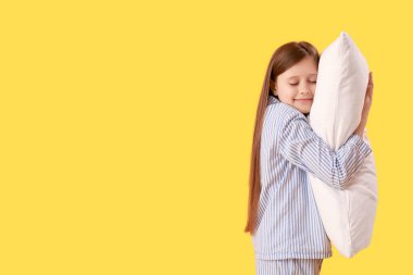 Küçük kız sarı arka planda yastığa sarılıyor.