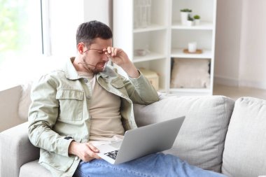 Evde dizüstü bilgisayar kullanmaktan bıkmış şık gözlükleri olan yakışıklı bir adam.