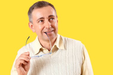 Sarı arka planda gözlüklü düşünceli olgun bir adam.