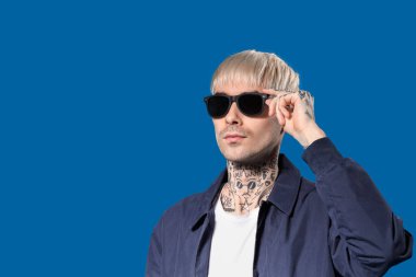 Mavi arka planda güneş gözlüklü genç adam.