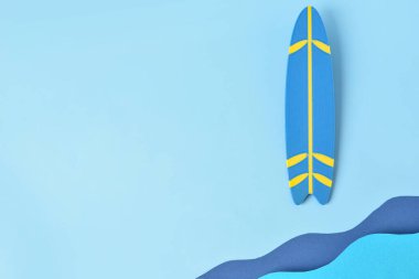 Mavi zemin üzerinde kağıt dalgaları ve mini sörf tahtası olan yaratıcı kompozisyon