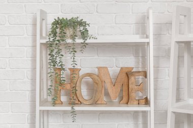 Beyaz tuğla duvarın yanında bitki ve dekor bulunan raf ünitesi