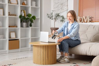 Oturma odasında, masada dizüstü bilgisayarla gayzer kahve makinesinden fincana espresso dolduran genç bir kadın.