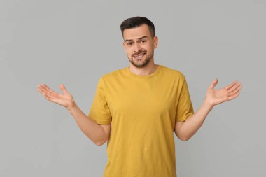 Yakışıklı, endişeli, gri arka planda omuz silken genç adam.