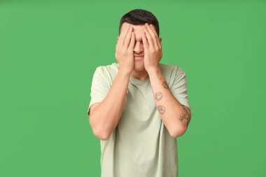 Yakışıklı, utangaç, elleri yeşil arka planda genç bir adam.