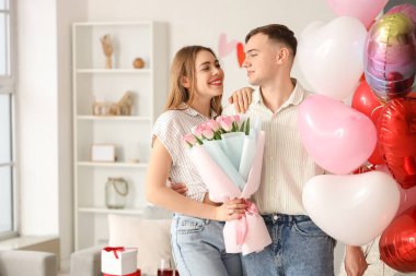 Kalp şeklinde balonları ve bir buket çiçekleri olan genç ve güzel bir çift sevgililer gününü evde kutluyor.