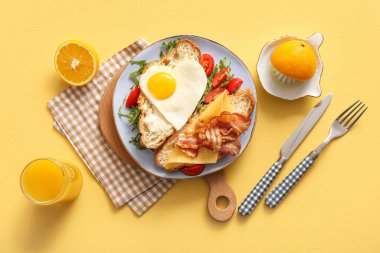 Lezzetli kızarmış yumurta, kruvasan, pastırma, domates ve sarı arka planda bir bardak meyve suyu.