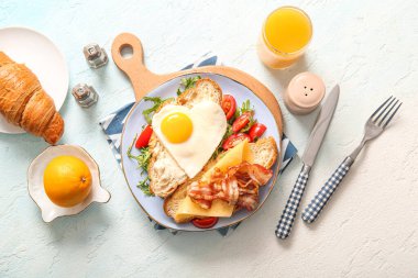 Lezzetli kızarmış yumurta, kruvasan, pastırma, tabakta domates ve arka planda bir bardak meyve suyu karışımı.