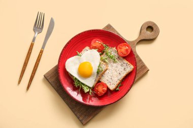 Lezzetli kızarmış yumurta, tost, domates, roka ve bej arkaplanlı çatal bıçak takımı.