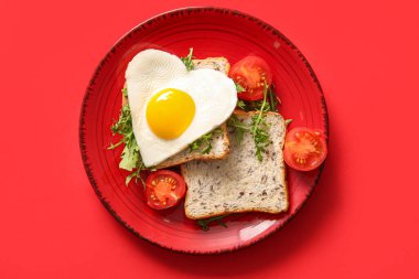 Kırmızı arka planda lezzetli yumurta, tost, domates ve roka tabağı.
