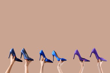 Bej arka planda farklı ayakkabılar tutan kadın eller.