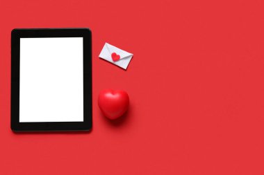 Kırmızı arka planda aşk mektubu ve kalbi olan bir tablet bilgisayar. Online randevu kavramı