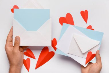 Zarflı erkek eller, boş kartlar ve beyaz arka planda kırmızı kağıt kalpler. Sevgililer Günü kutlaması