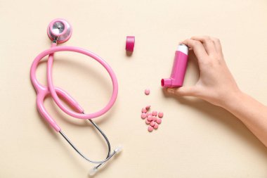 Astım spreyi, steteskop ve bej arka planda haplarla çocuk eli.