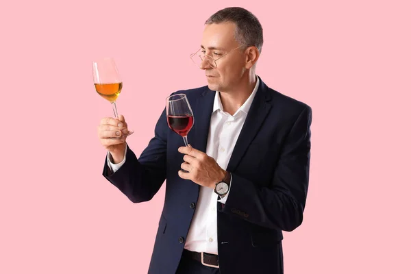 Mature man with glasses of wine on pink background