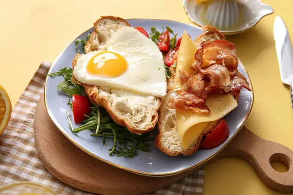 Lezzetli kızarmış yumurta, kruvasan, pastırma, domates ve roka ile bej arka planda, yakın plan