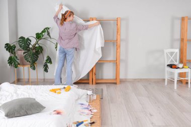 Yatak odası ve arka manzara tamiri sırasında rafa bakan genç bir kadın.