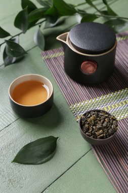 Bambu hasırı, bir fincan lezzetli çay, çaydanlık ve yeşil arka planda yaprakları olan kâse.