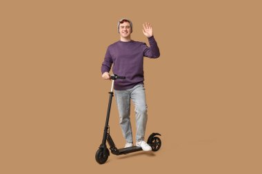 Kahverengi arka planda modern elektrikli scooter kullanan genç bir adam.