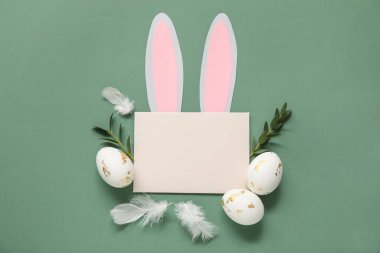 Kağıttan yapılmış tavşan kulaklı boş kart, Paskalya yumurtaları, tüyler ve yeşil arka planda yapraklar