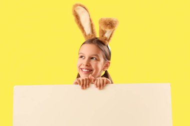 Paskalya tavşanı kulakları ve sarı arka planda boş posteri olan sevimli küçük bir kız.