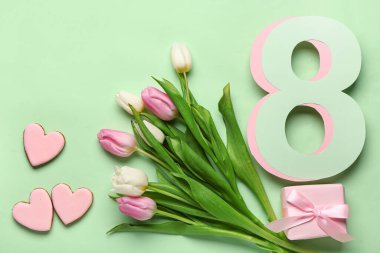 Lale çiçekleri, hediye kutusu ve yeşil arka planda kurabiyeleri olan kağıttan yapılmış 8 figür. Uluslararası Kadınlar Günü kutlamaları