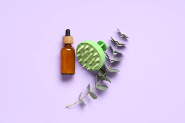 Saç derisi masaj aleti ve eflatun arka planında bir şişe kozmetik yağı ve okaliptüs.