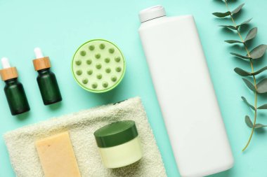 Mavi arka planda farklı kozmetik ürünleri, havlu ve okaliptüs içeren saç masajı aleti.