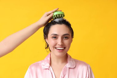 Sarı arka planda saç derisi masaj aleti olan güzel genç bir kadın ve el.